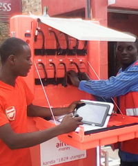A franchisee of the M.S.K making use of the tablet provided to allow the sales of services electronically. Behind him is the M.S.K itself equipped with multiple ports to charge small electronics.